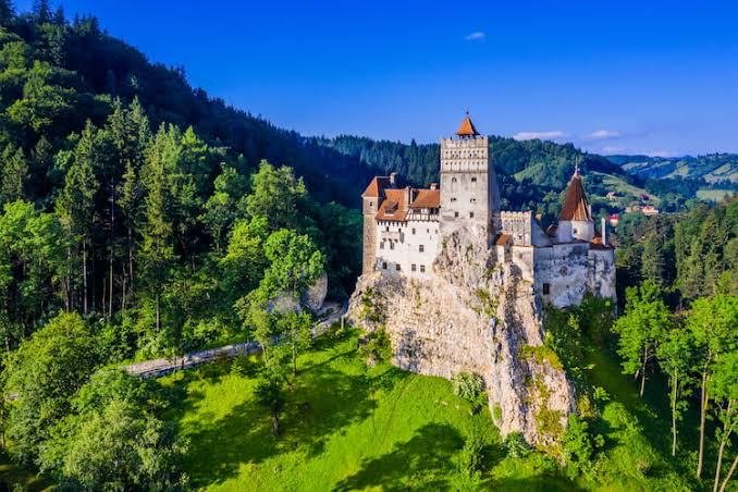 Aerial view of Bran Castle on a rocky outcrop surrounded by green forest