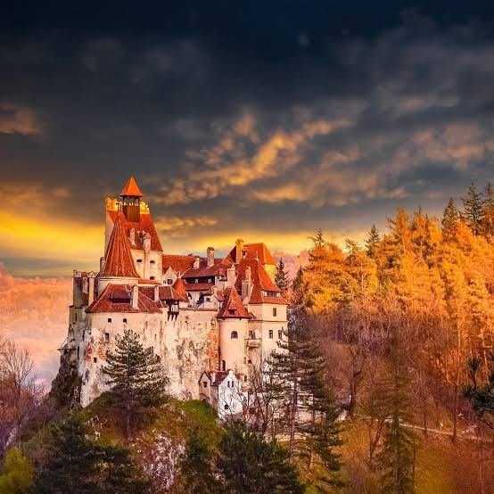 Bran Castle at sunset with golden autumn trees and dramatic clouds
