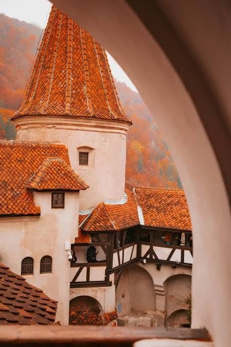 Bran Castle tower with terracotta roof framed by a stone archway, autumn forest behind