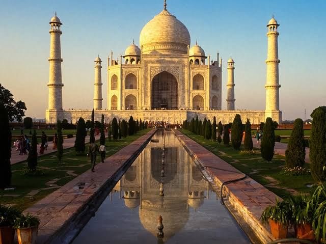 The Taj Mahal glowing gold in warm evening light, reflected in the pool